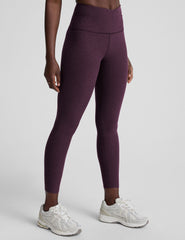 model wearing purple high-waisted midi length leggings with a front crossover detail on the waistband on a plain background.