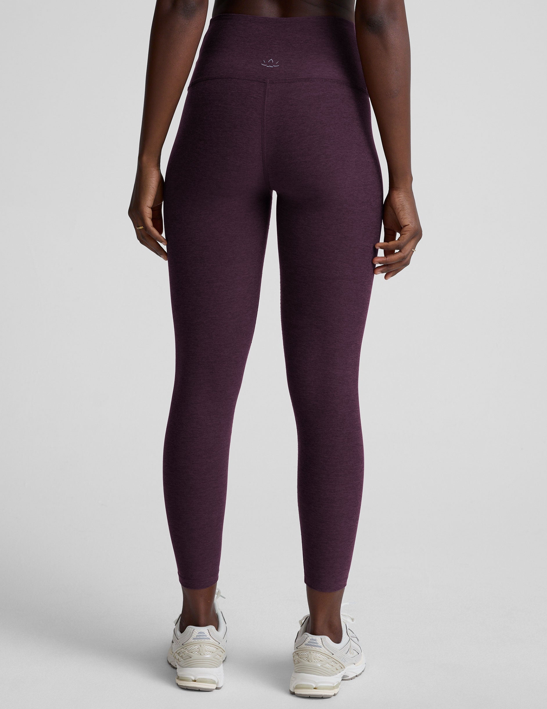 model wearing purple high-waisted midi length leggings with a front crossover detail on the waistband on a plain background.