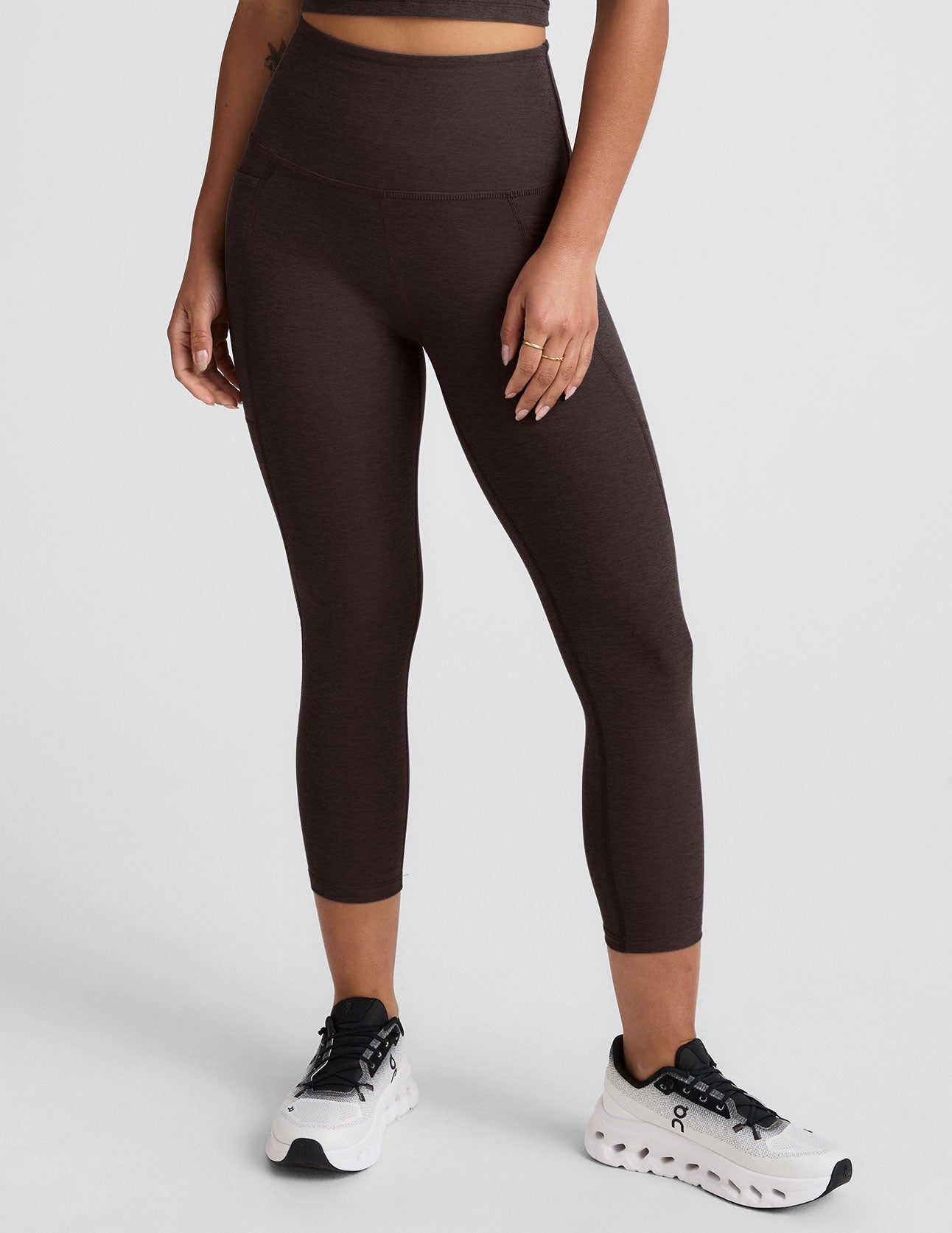 woman wearing a brown capri length leggings with pockets on a plain background.