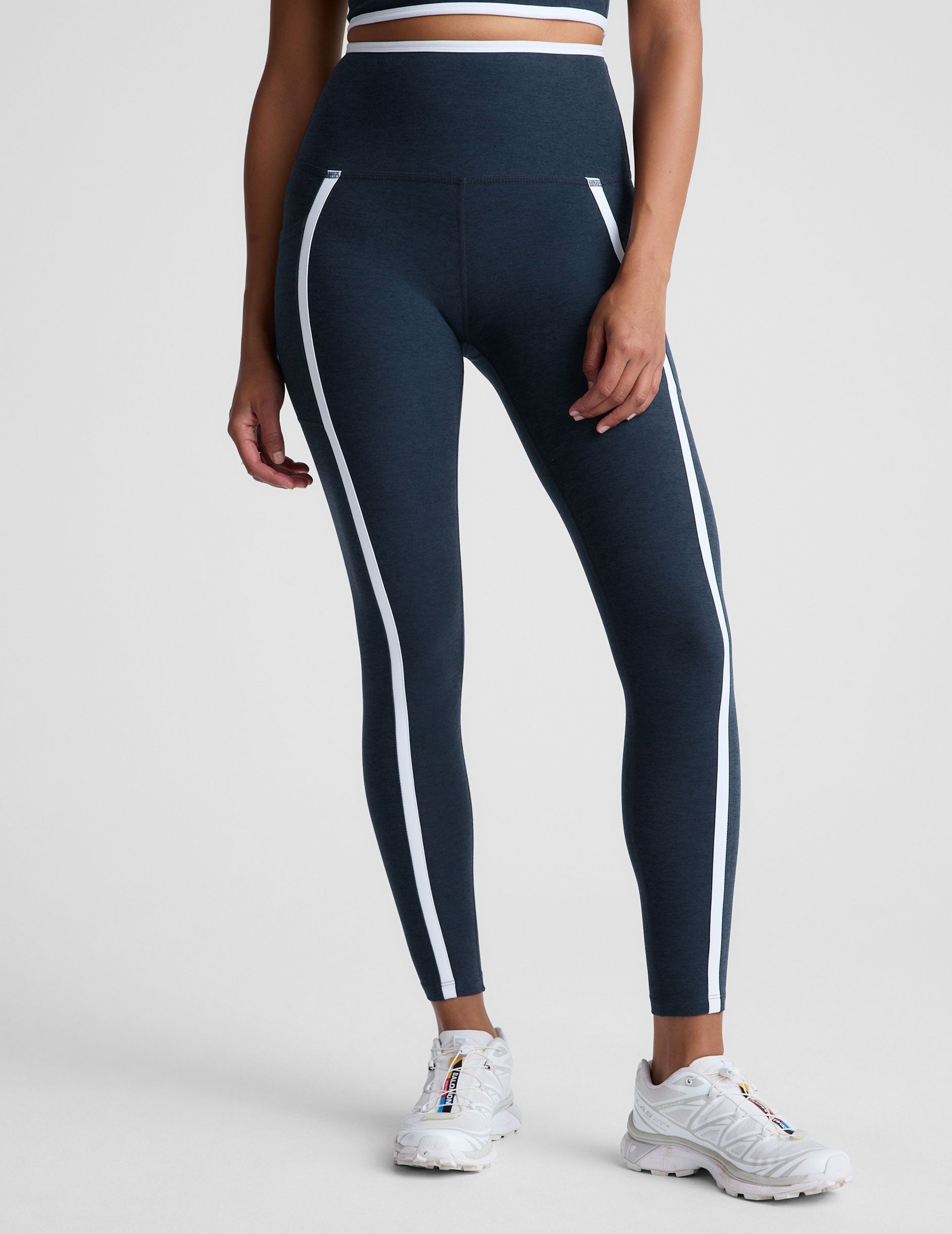 blue high-waisted midi length leggings with pockets and white piping.