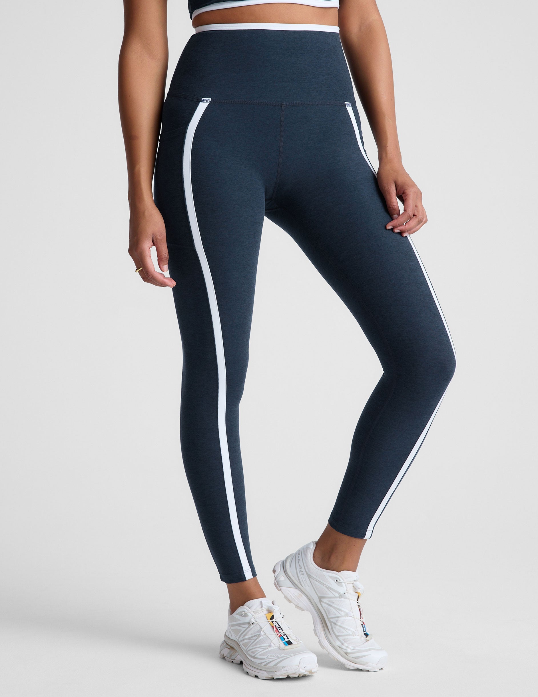 blue high-waisted midi length leggings with pockets and white piping.