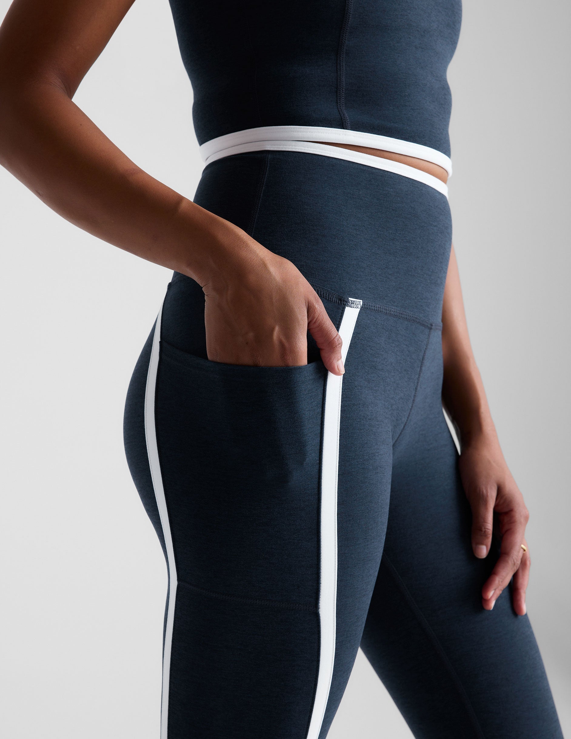 blue high-waisted midi length leggings with pockets and white piping.