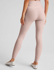 model wearing a pink cropped tank top and pink high-waisted midi length leggings on a plain background.