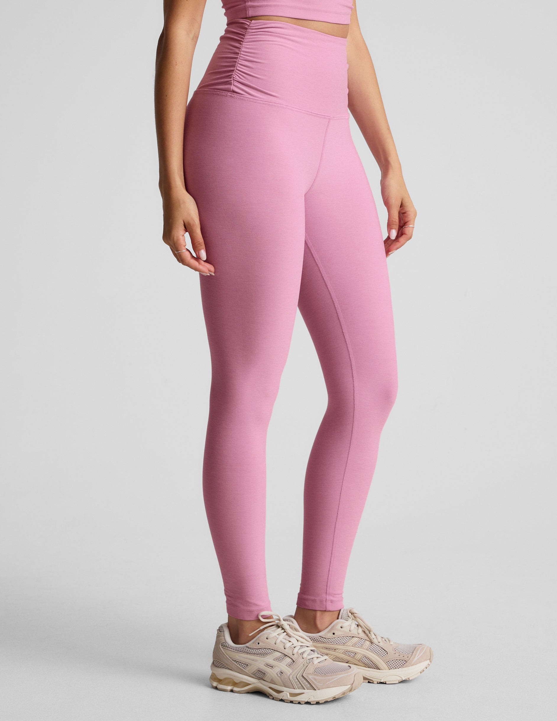 pink high-waisted midi length leggings with shirred detailing on the side of each waistband.
