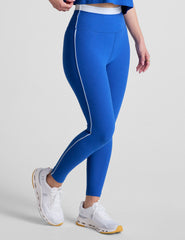 blue high-waisted midi leggings with white contrast piping on side of leg and around waistband.