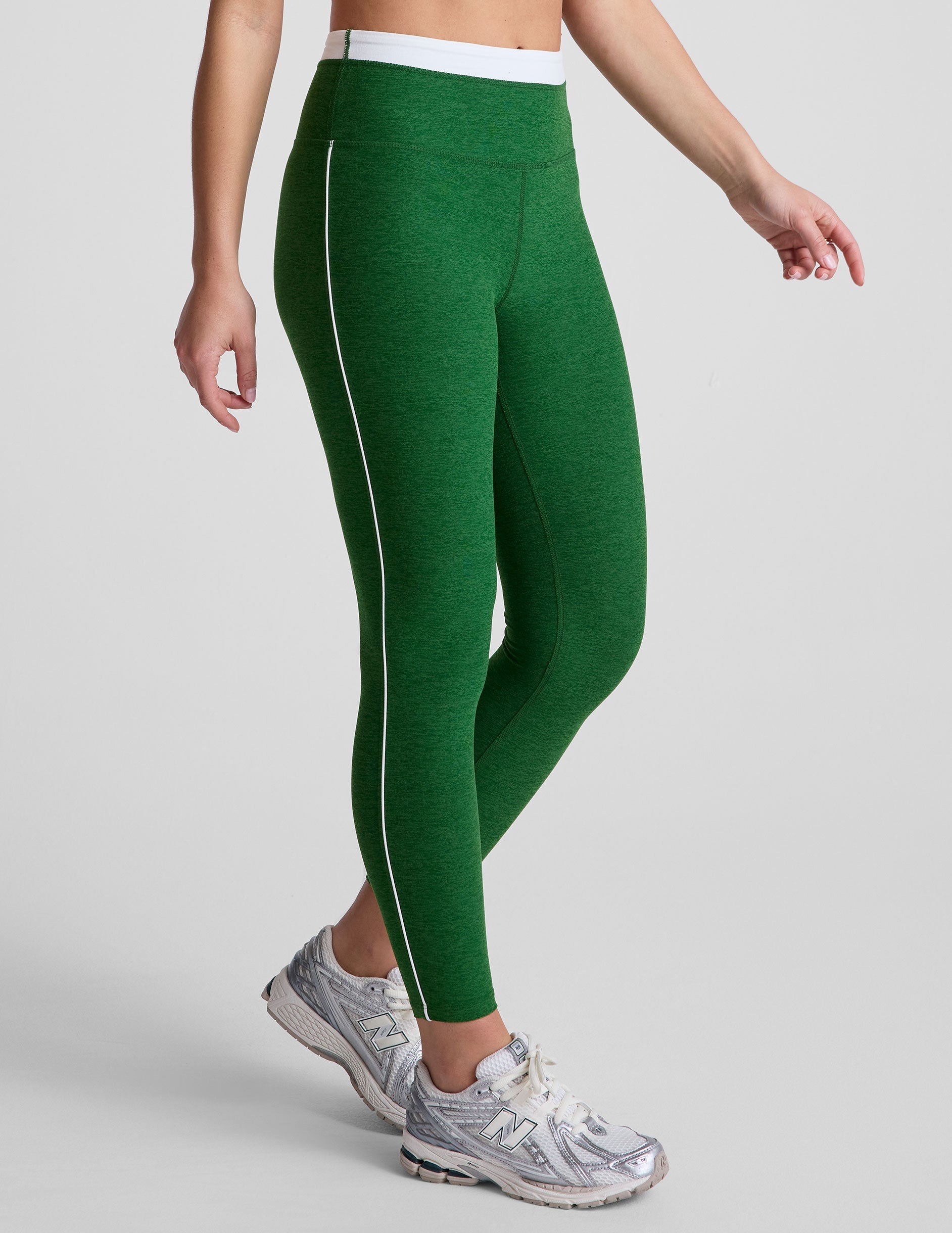 green high-waisted midi leggings with white contrast piping on side of leg and around waistband.