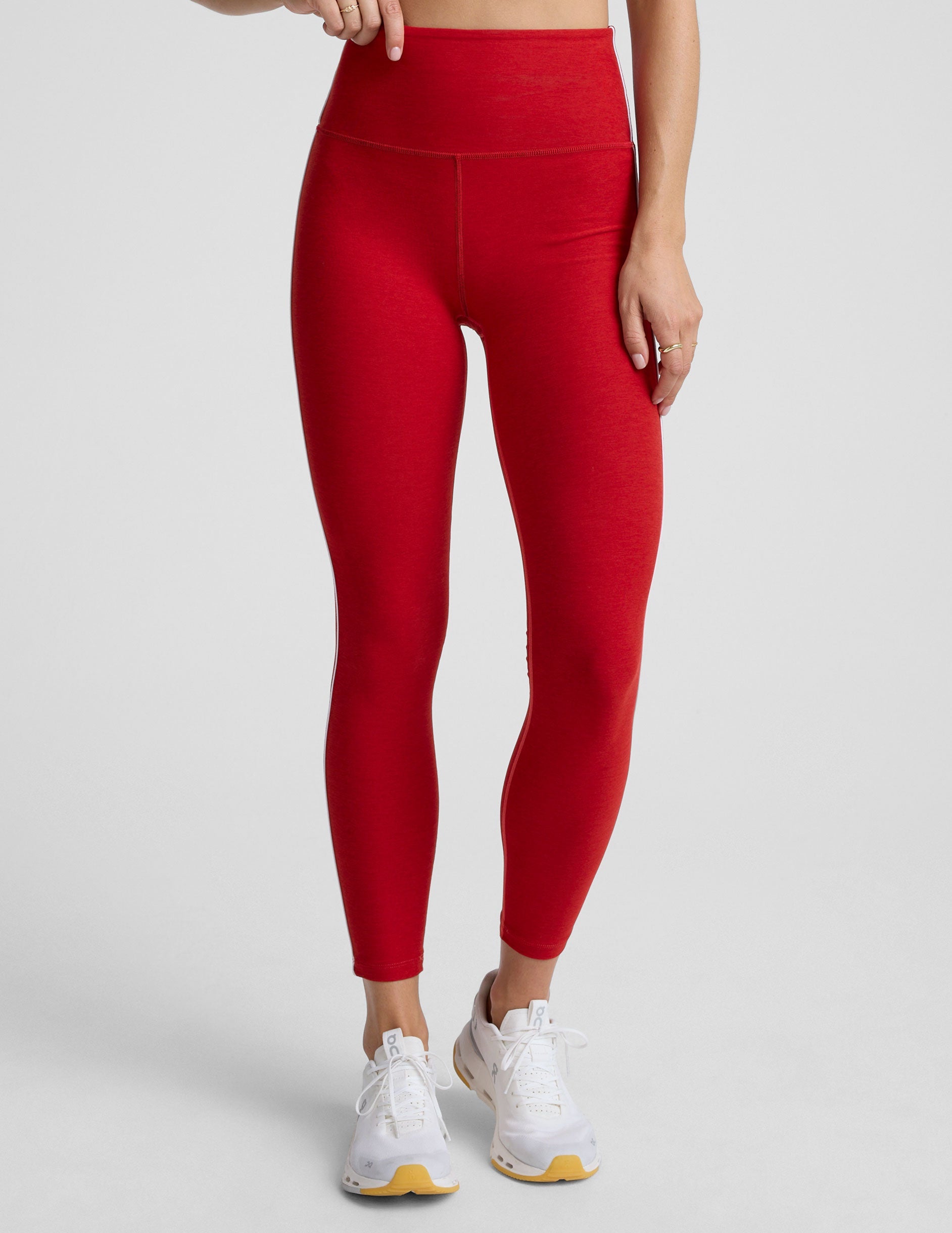 woman in red bra with white piping and red high-waisted midi length leggings with white piping against a plain background.