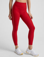 woman in red bra with white piping and red high-waisted midi length leggings with white piping against a plain background.