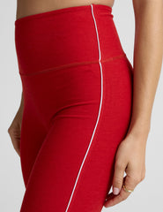 woman in red bra with white piping and red high-waisted midi length leggings with white piping against a plain background.