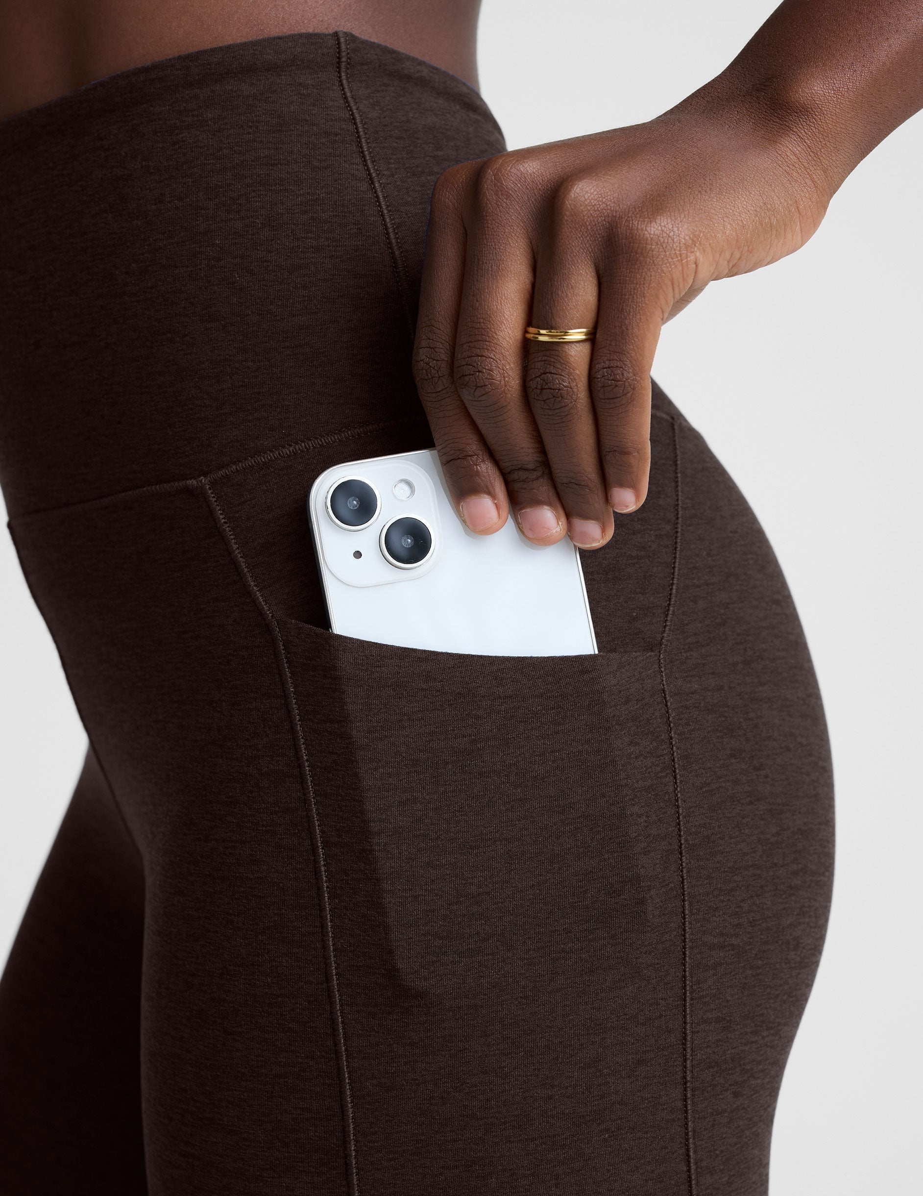 person wearing brown leggings with a pocket holding a white phone.