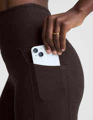 person wearing brown leggings with a pocket holding a white phone.