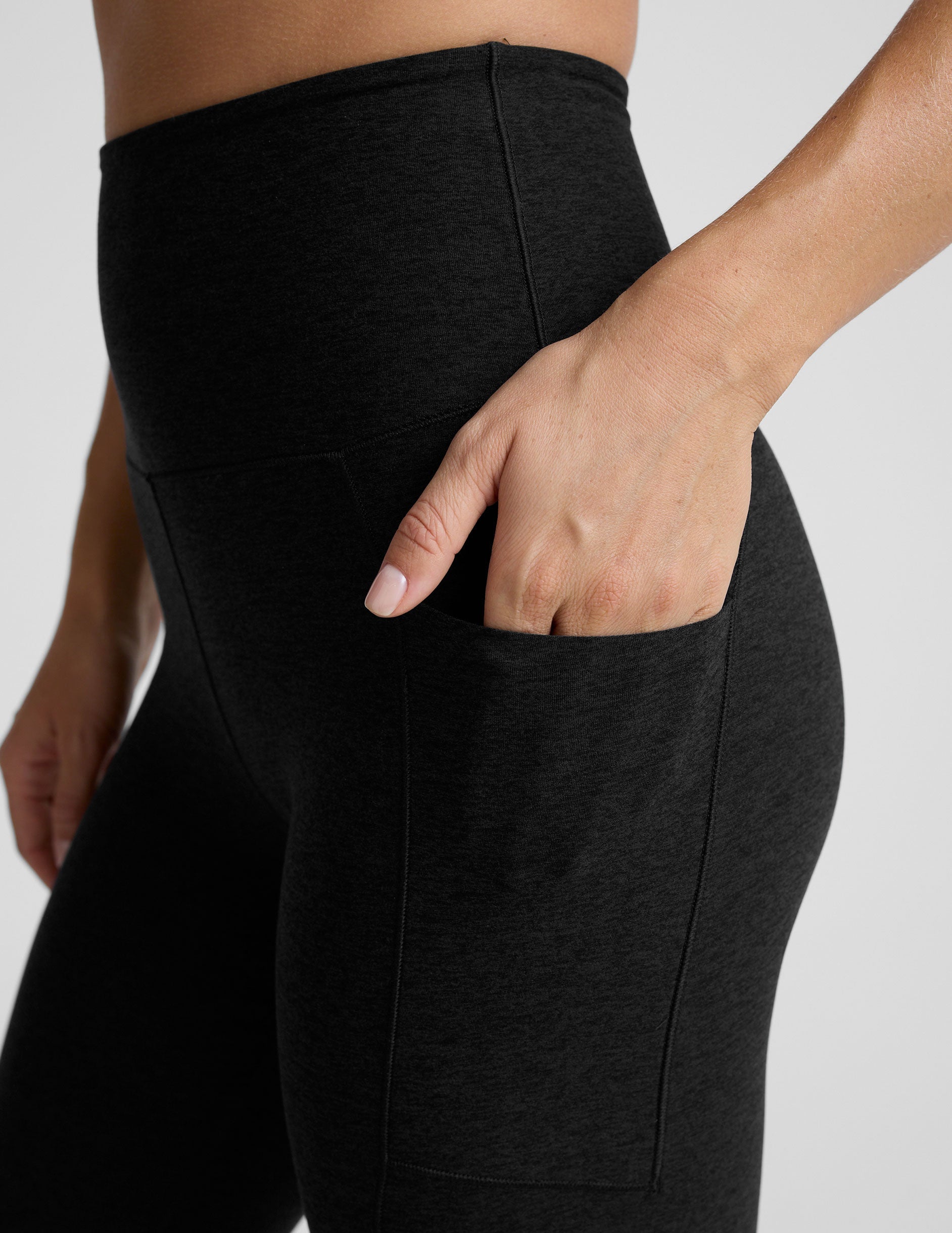 model wearing black midi length leggings with 3 pockets against a plain background.