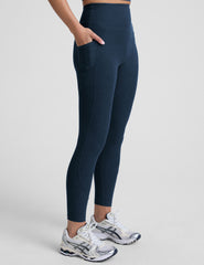 model wearing blue midi length leggings with 3 pockets against a plain background.