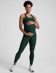 pregnant woman wearing a green tank top and leggings on a plain background.