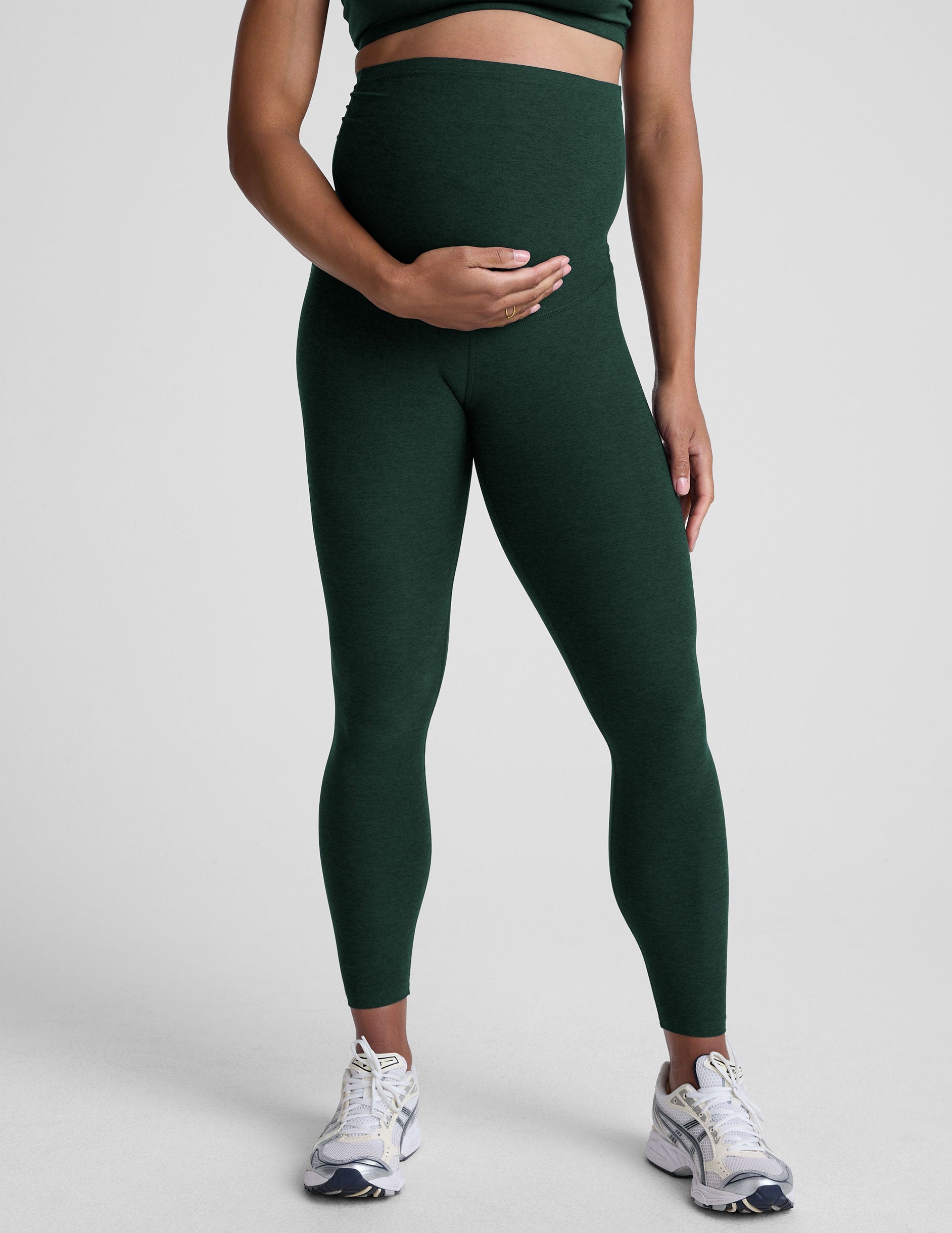 pregnant woman wearing green maternity leggings on a plain background.