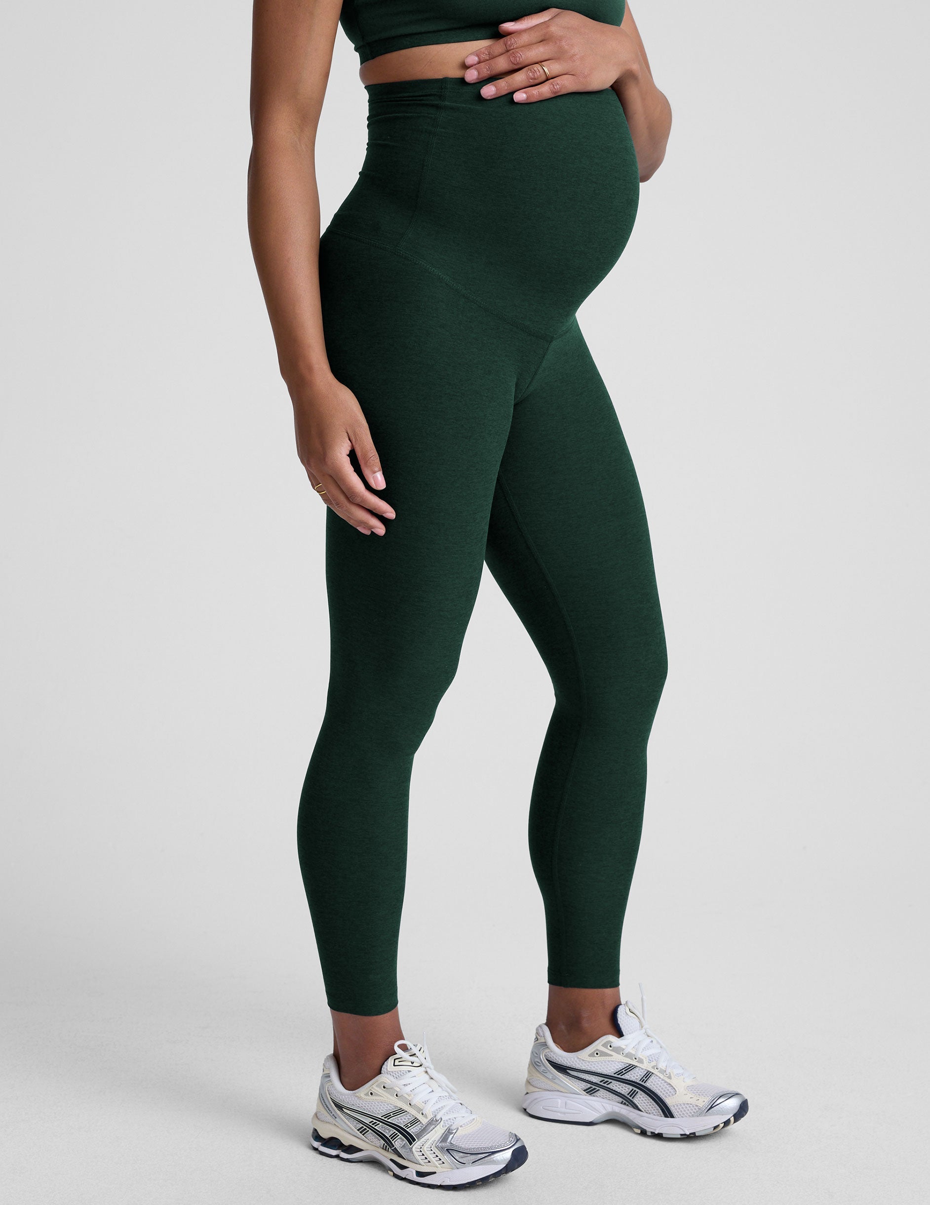 pregnant woman wearing green maternity leggings on a plain background.