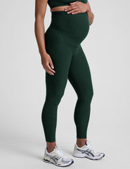 pregnant woman wearing green maternity leggings on a plain background.