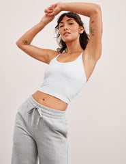 model wearing a white crop top and gray sweatpants against a plain background.