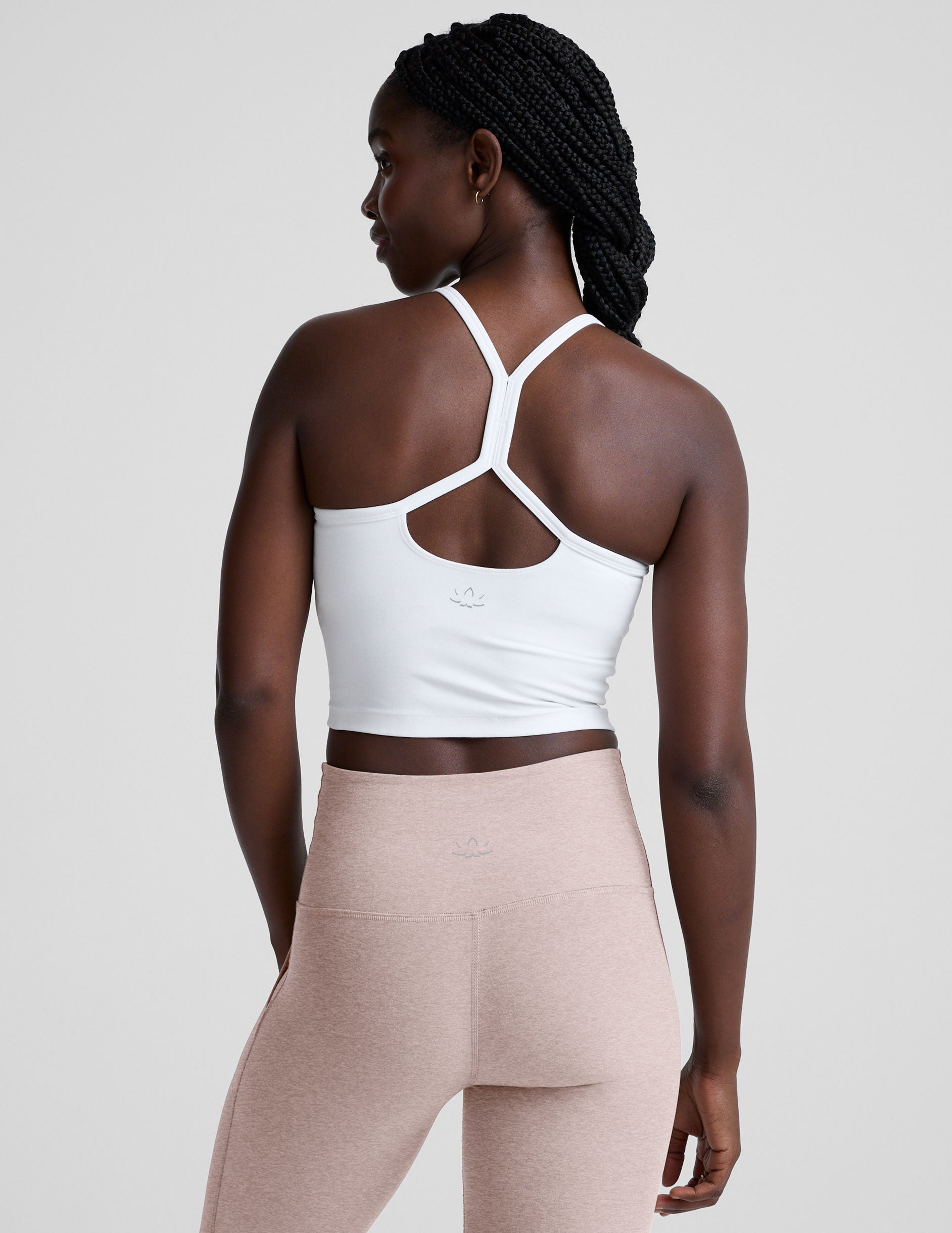 woman wearing a white racerback cropped tank and pink pants against a plain background.