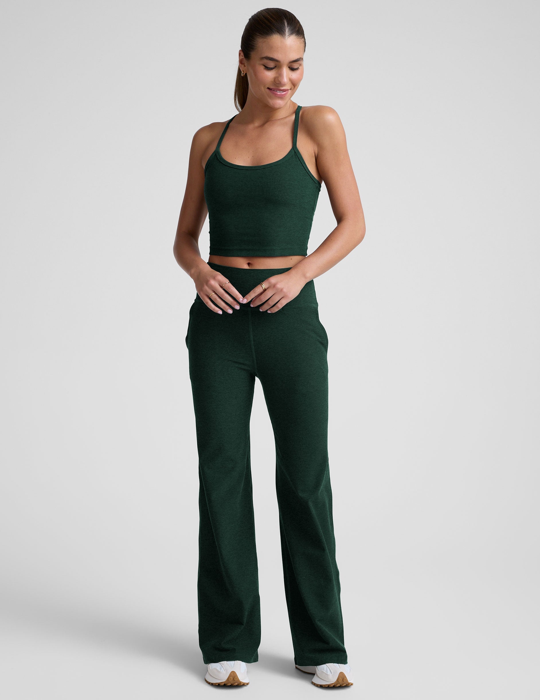 woman wearing a green racerback cropped tank top and pants against a plain background.