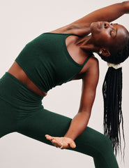 woman wearing a green racerback cropped tank top and leggings against a plain background.