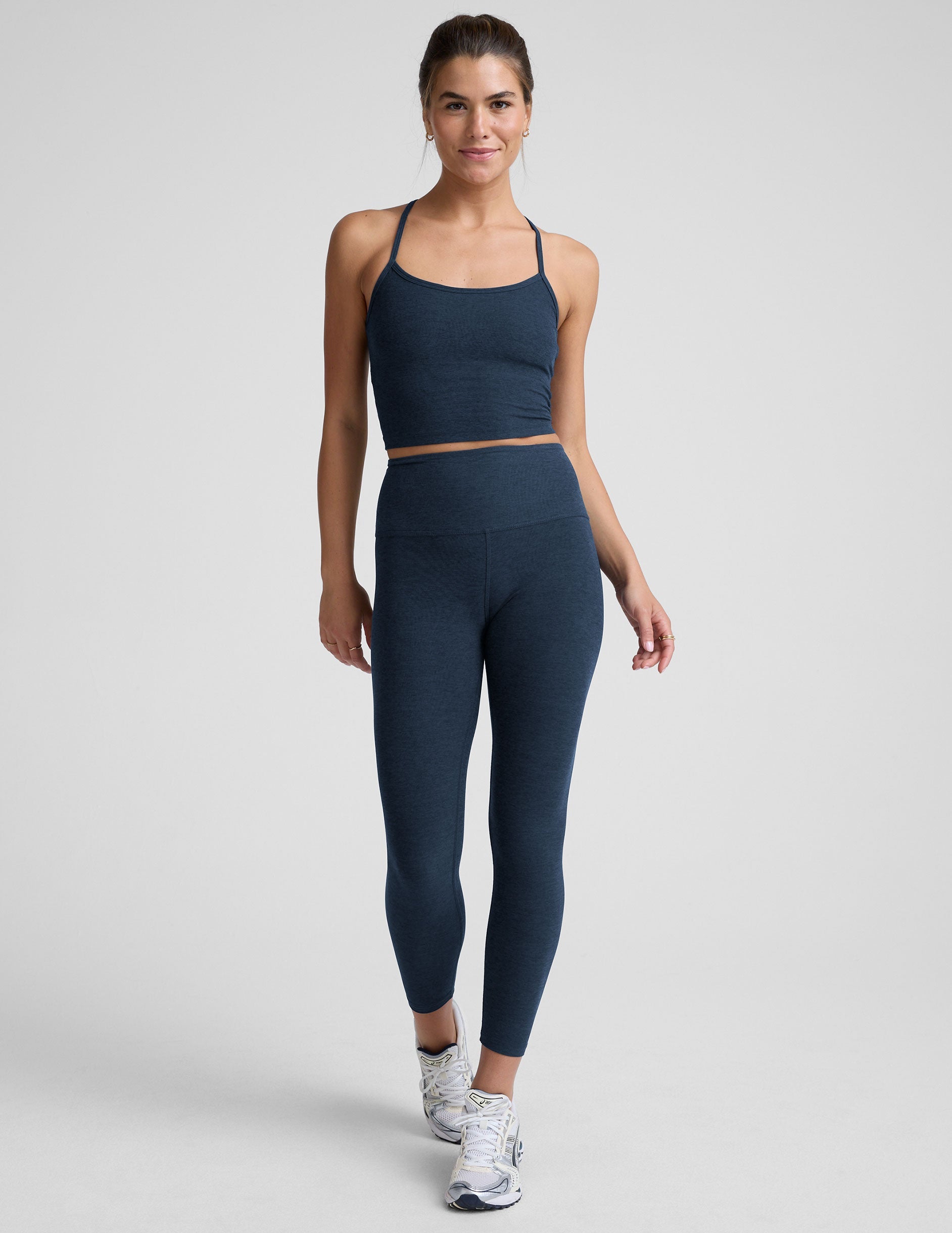 woman wearing a navy blue racerback cropped tank and leggings on a plain background.