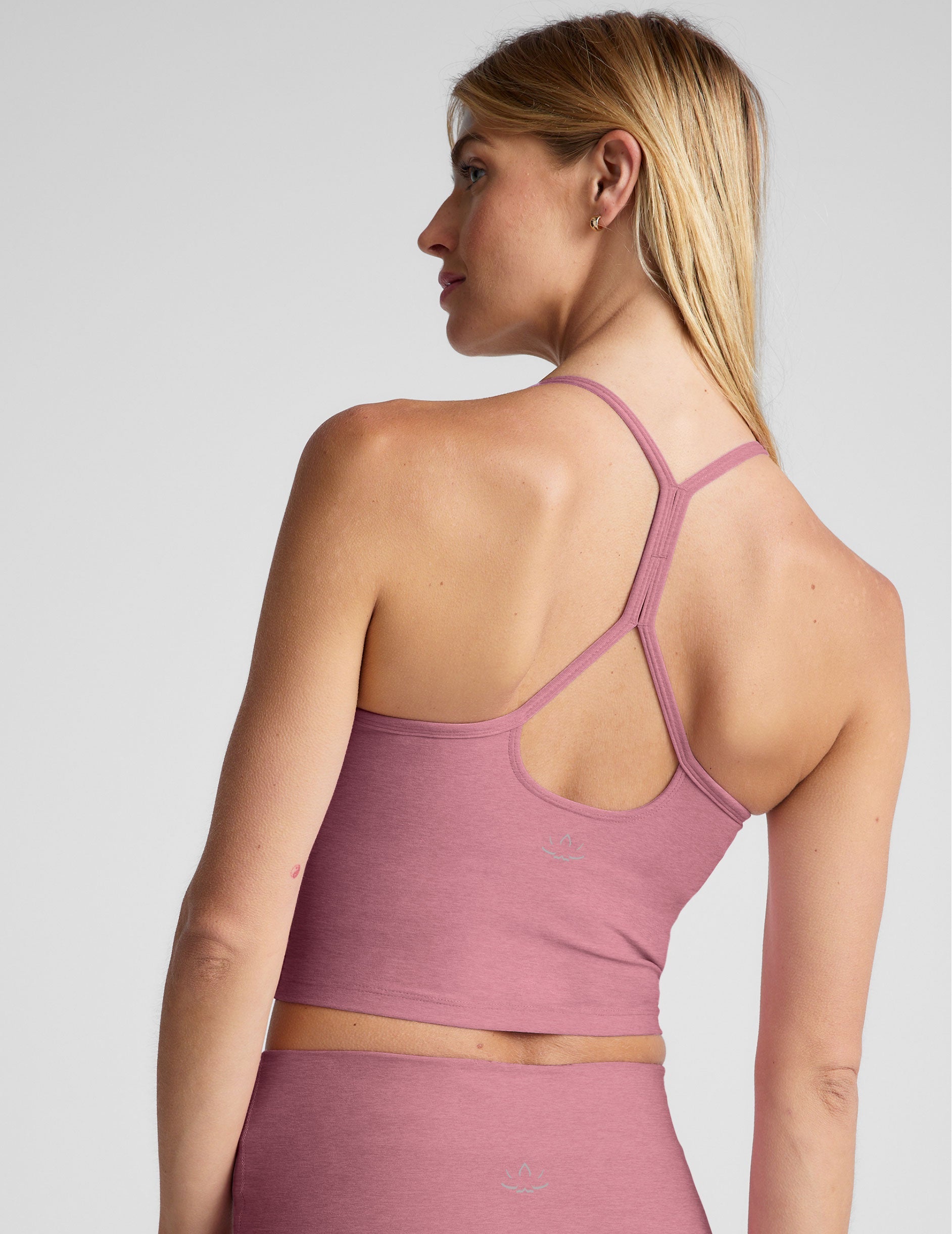 model wearing a pink racerback cropped tank top against a plain background.