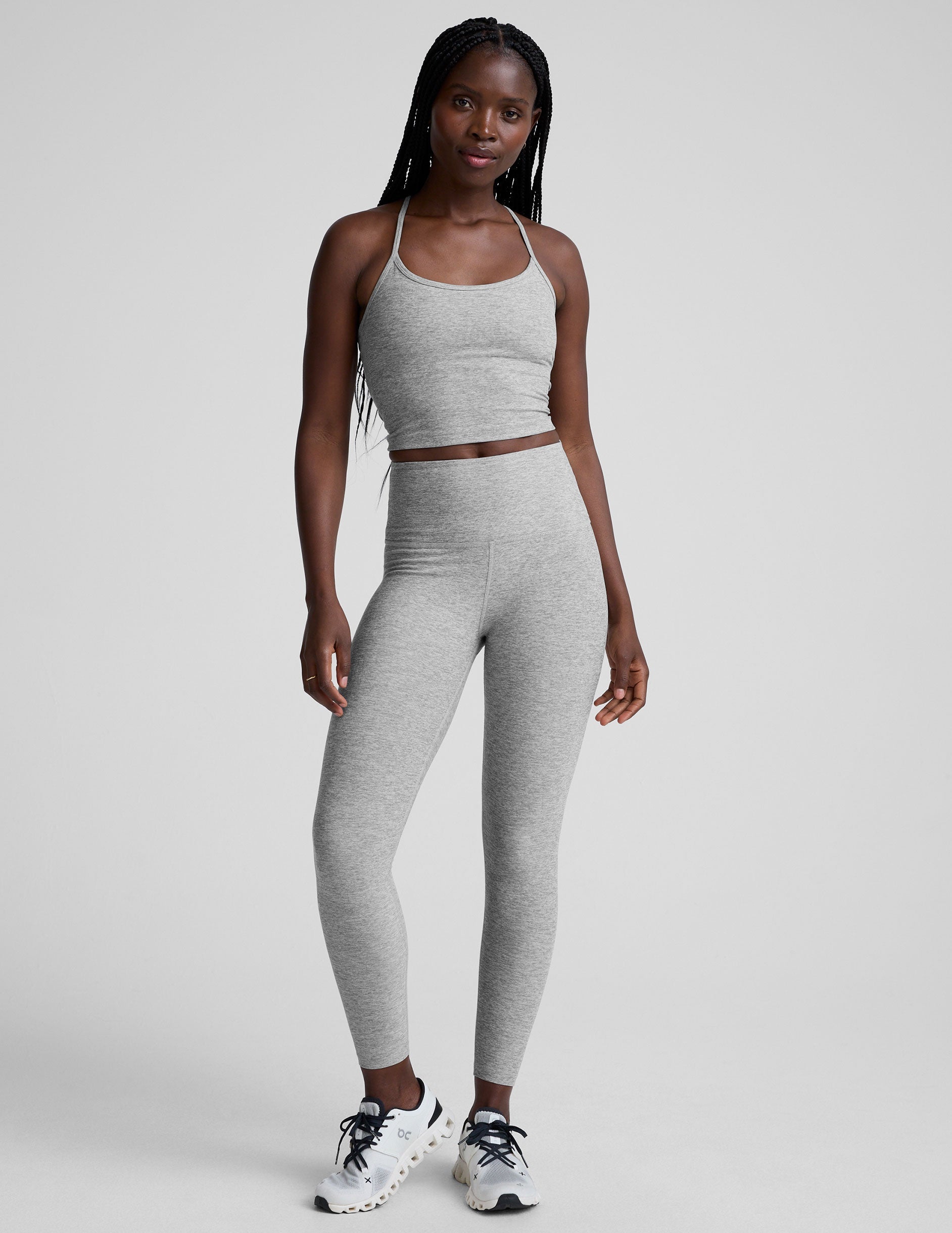 woman is wearing a gray racerback cropped tank and gray leggings against a plain background.
