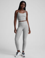 woman is wearing a gray racerback cropped tank and gray leggings against a plain background.