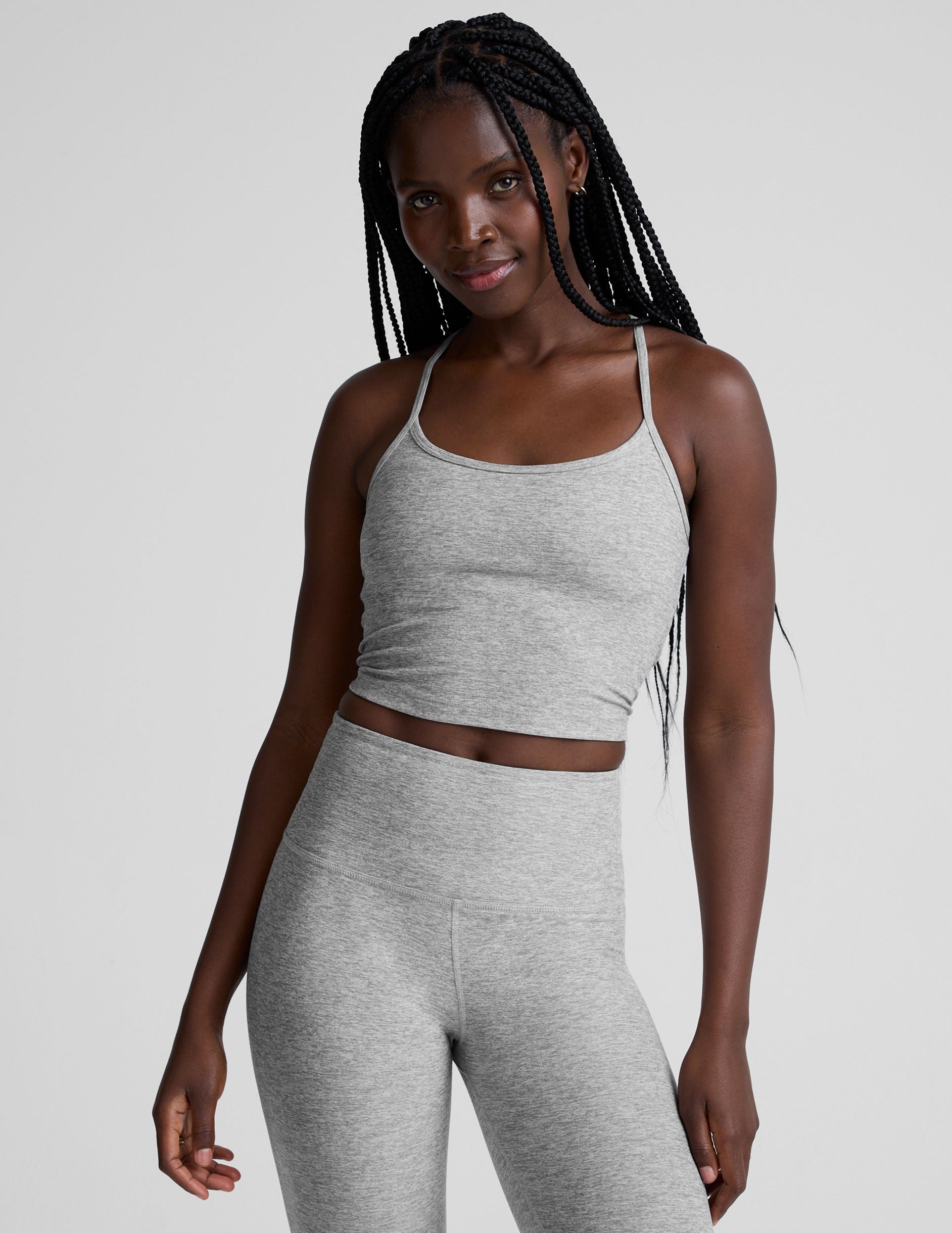 woman is wearing a gray racerback cropped tank and gray leggings against a plain background.