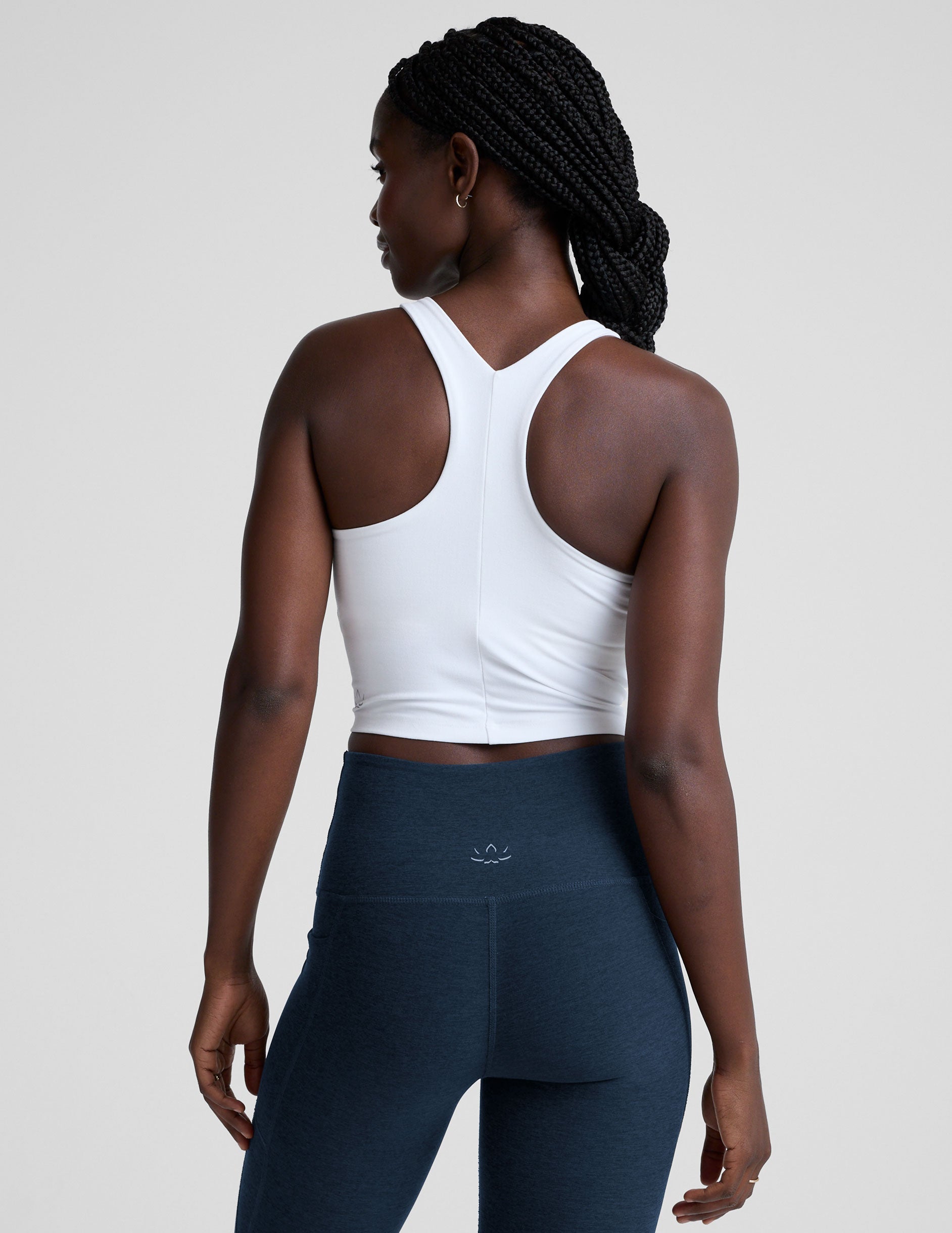 woman wearing a white high-neck racerback cropped tank and navy leggings on a plain background.