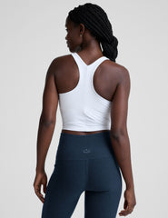 woman wearing a white high-neck racerback cropped tank and navy leggings on a plain background.