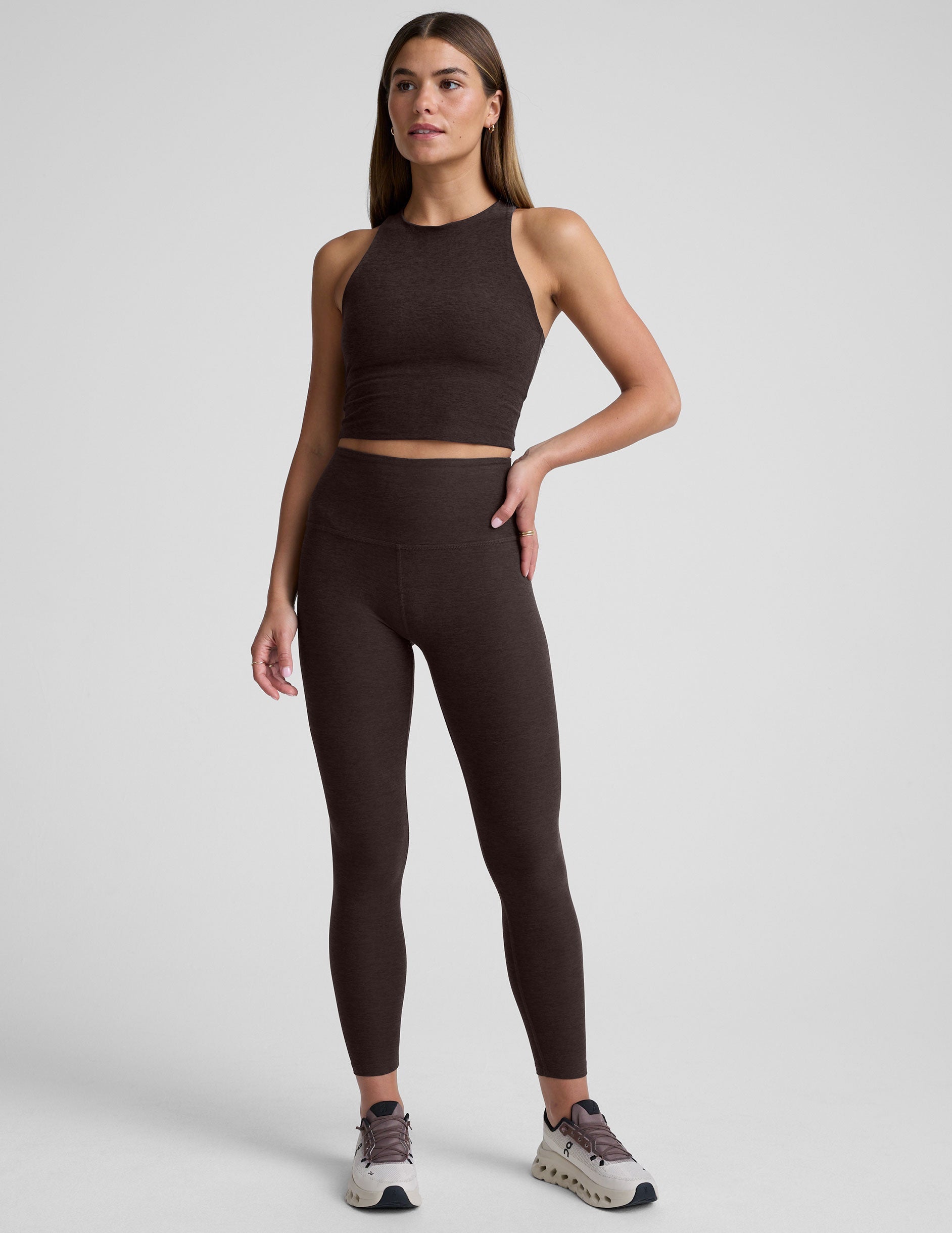 woman wearing a brown high neck racerback cropped tank and leggings on a plain background.