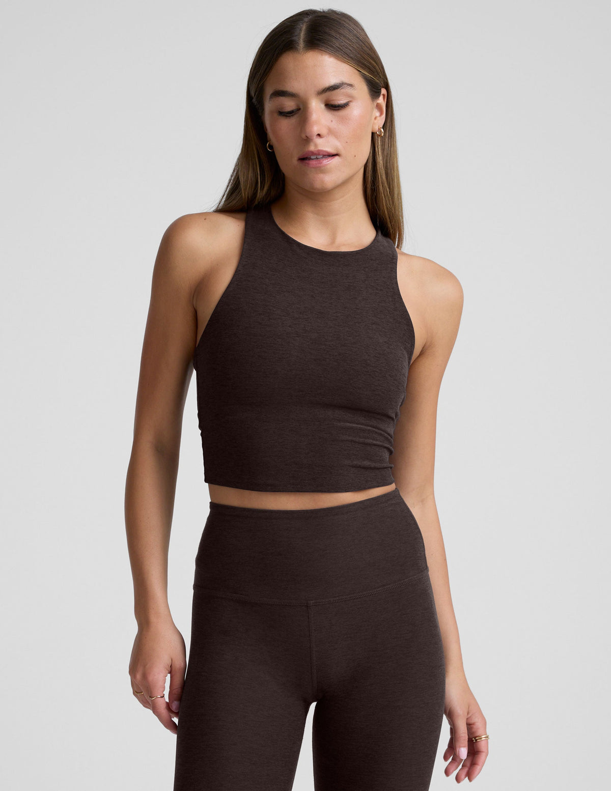 woman wearing a brown high neck racerback cropped tank and leggings on a plain background.