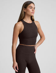 woman wearing a brown high neck racerback cropped tank and leggings on a plain background.