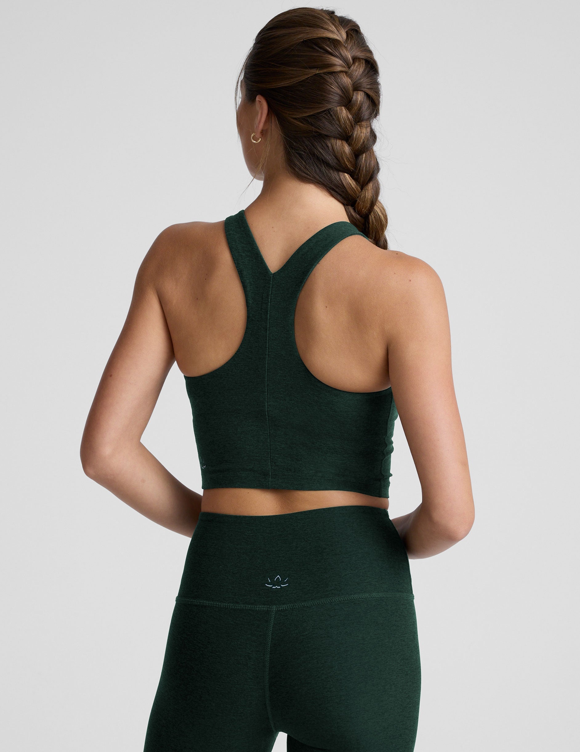 woman wearing a green high-neck racerback cropped tank and leggings on a plain background.