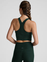 woman wearing a green high-neck racerback cropped tank and leggings on a plain background.