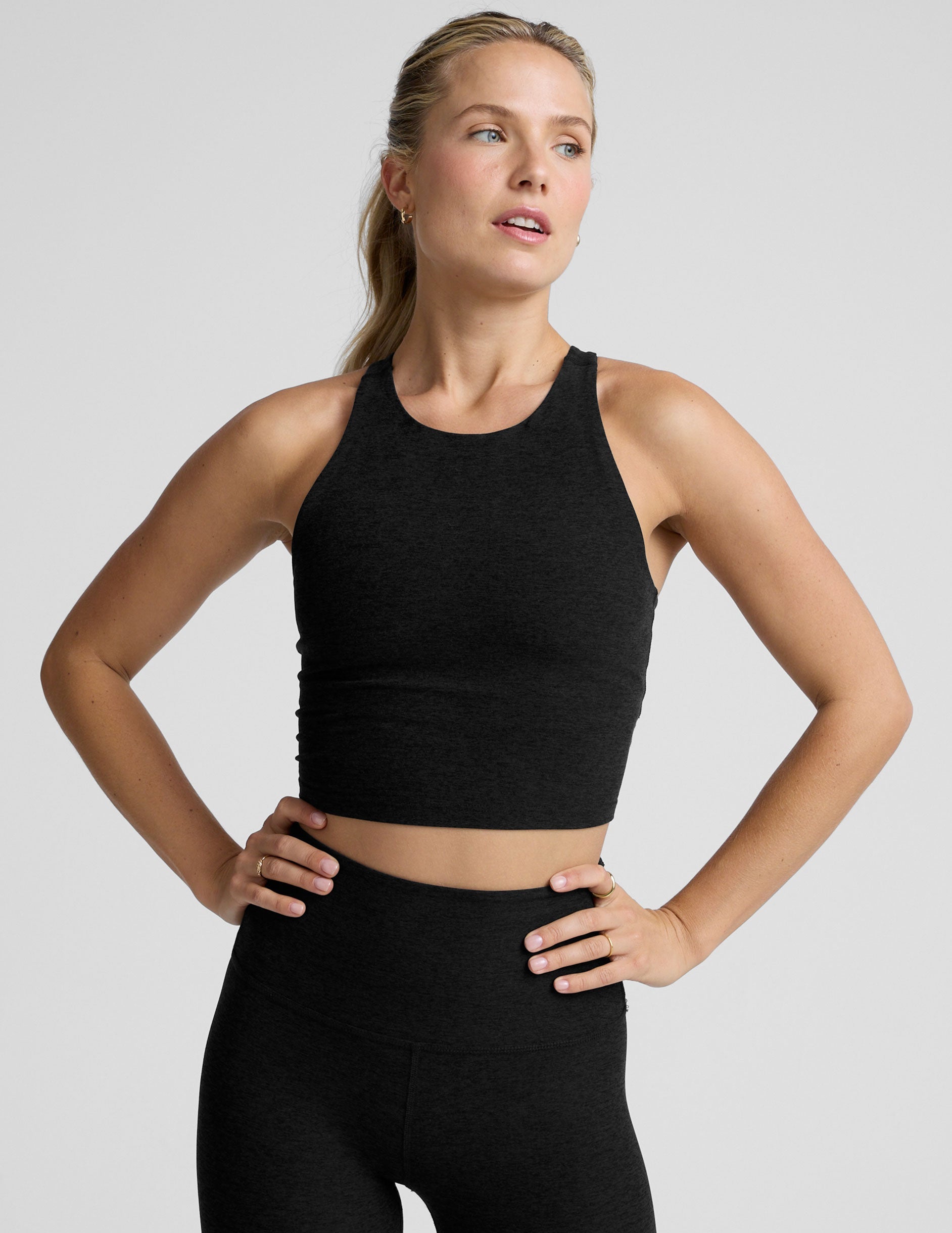 woman wearing a black high neck racerback cropped tank on a plain background.