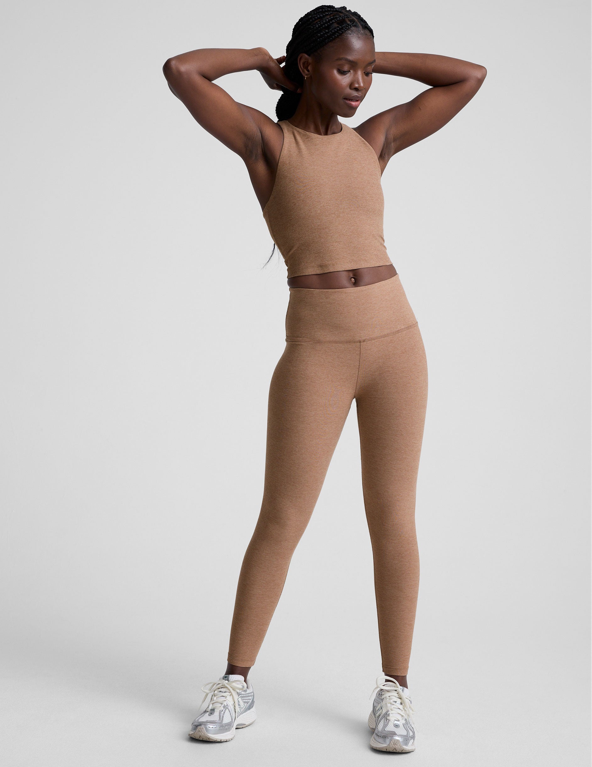 woman wearing a brown high neck racerback cropped tank top and leggings on a plain background.