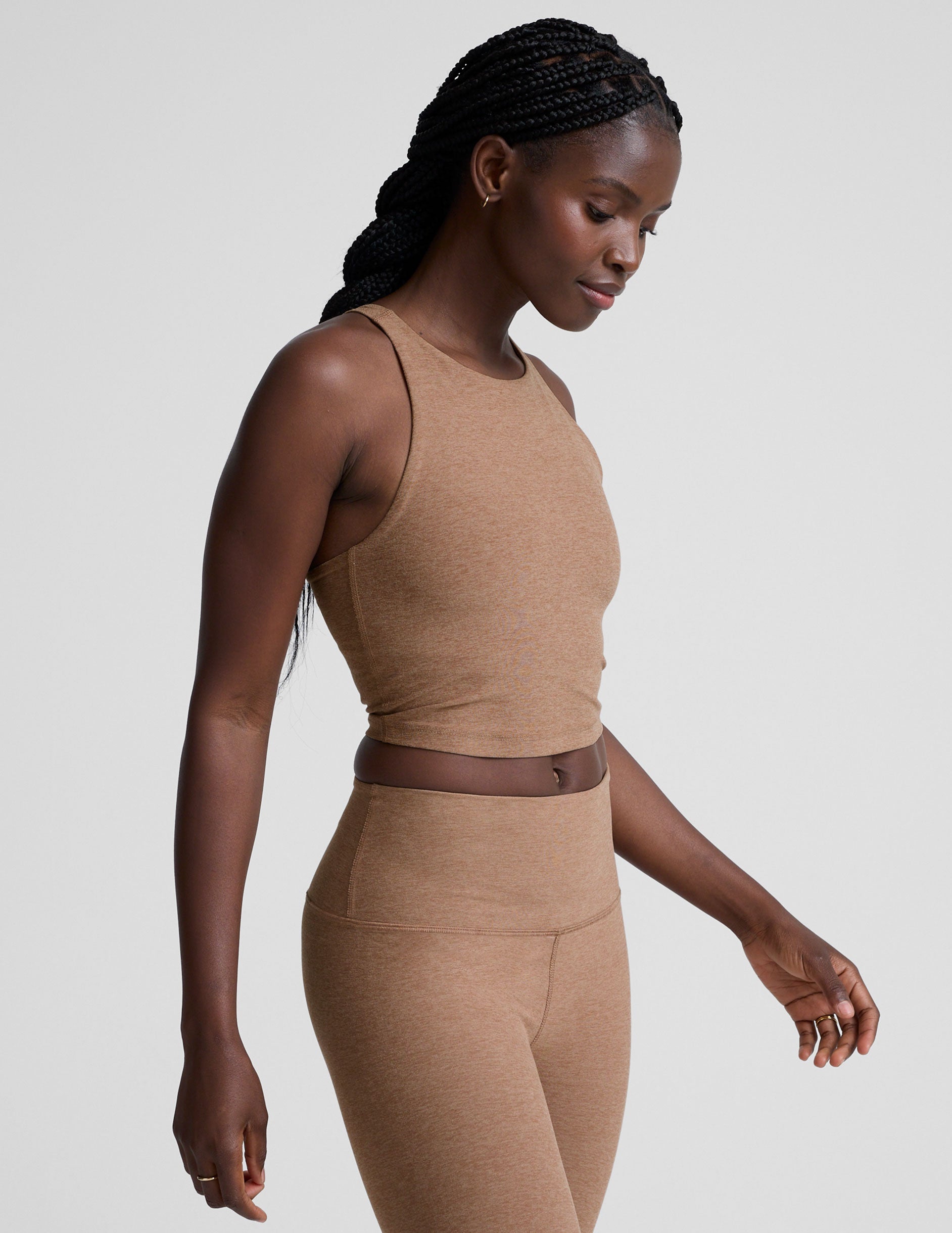 woman wearing a brown high neck racerback cropped tank top and leggings on a plain background.