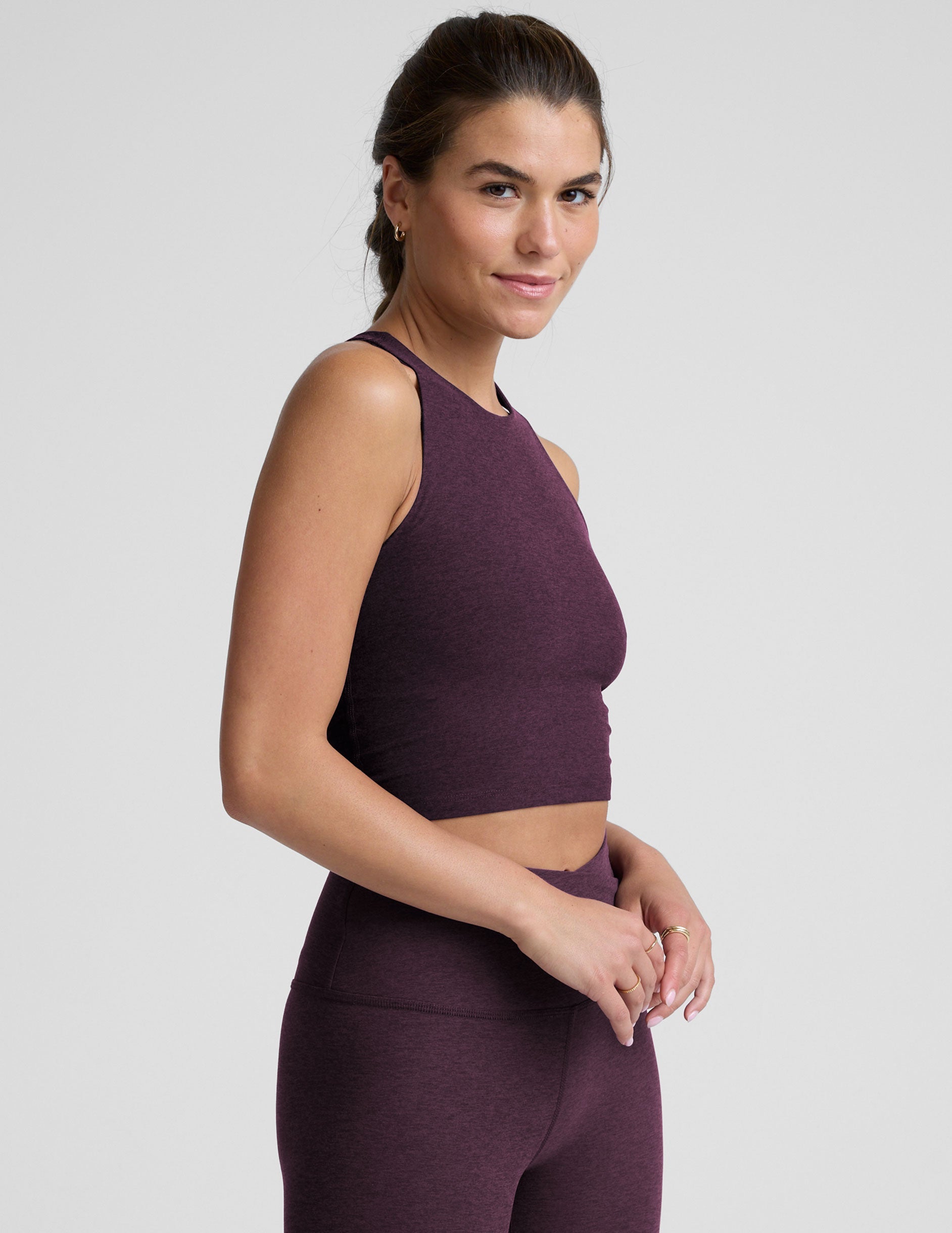 model wearing a purple high neck racerback cropped tank top and purple high-waisted midi length leggings against a plain background.
