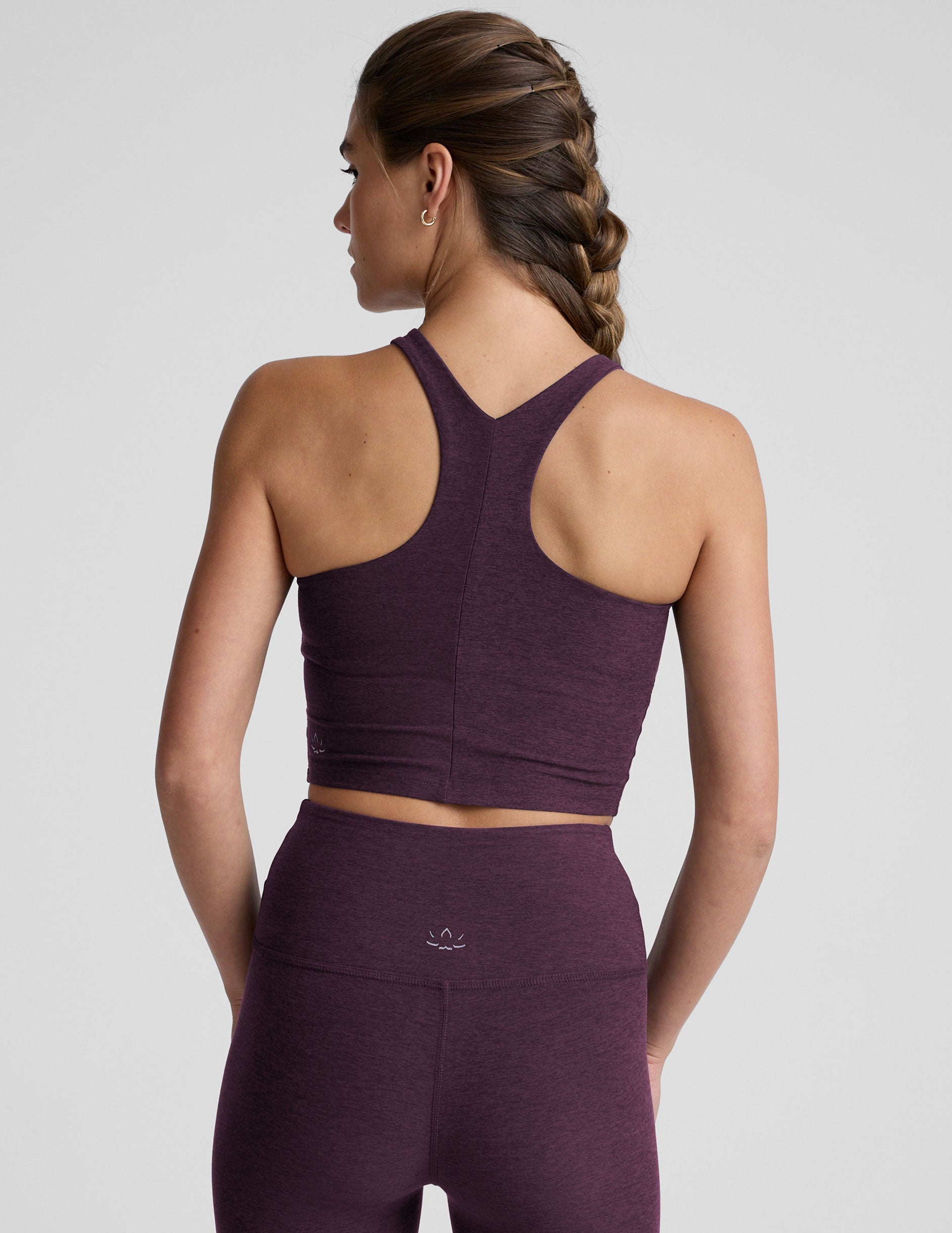 model wearing a purple high neck racerback cropped tank top and purple high-waisted midi length leggings against a plain background.