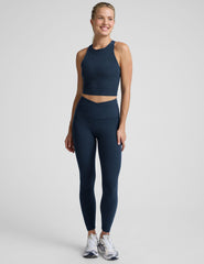 woman wearing a navy blue high neck cropped tank and leggings on a plain background.