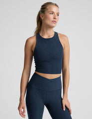 woman wearing a navy blue high neck cropped tank and leggings on a plain background.
