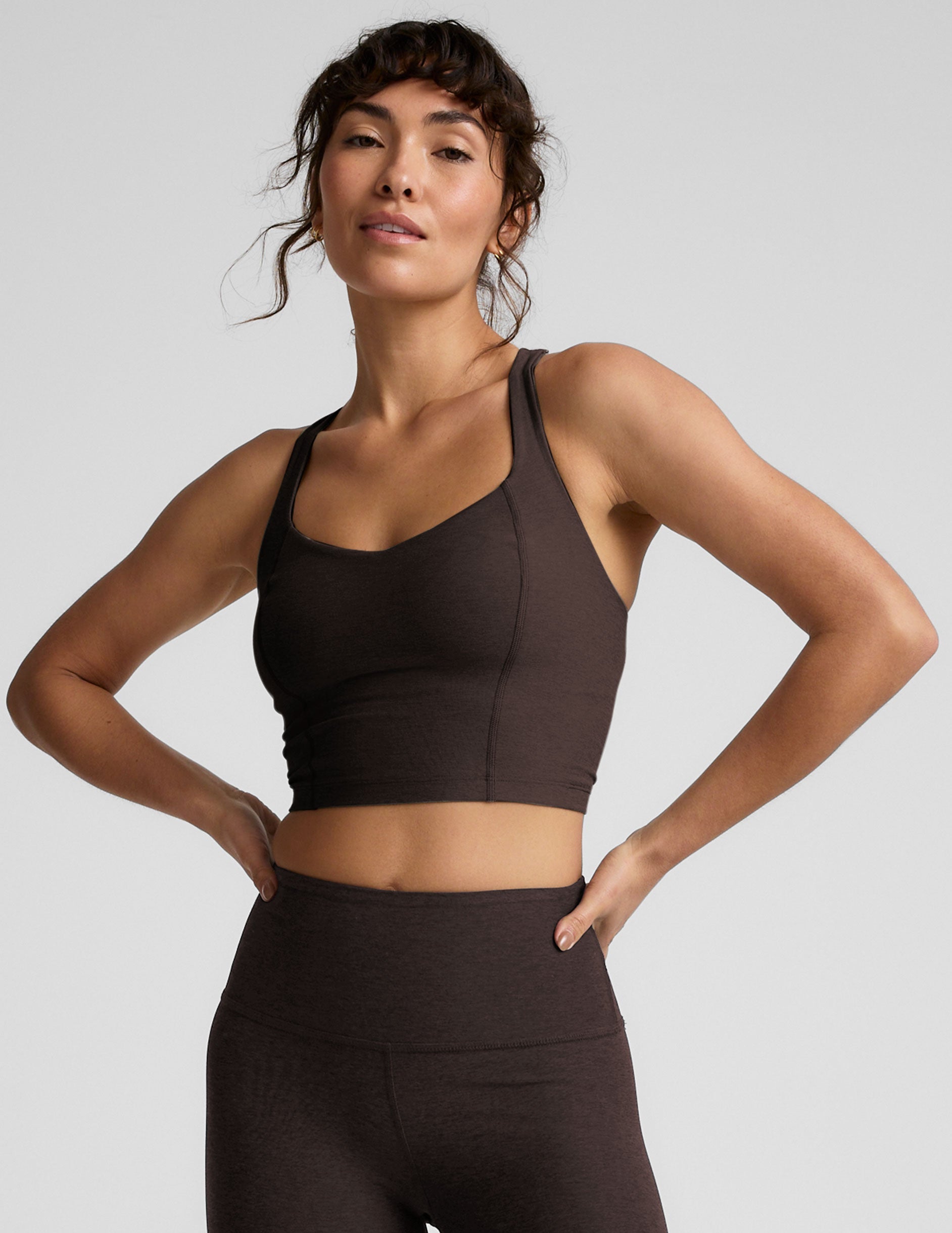 Woman in brown v-neck cropped racerback tank and brown leggings against a plain background.