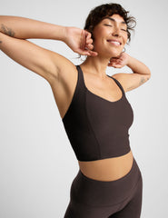 Woman in brown v-neck cropped racerback tank and brown leggings against a plain background.