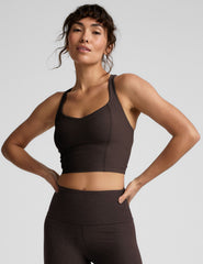 Woman in brown v-neck cropped racerback tank and brown leggings against a plain background.