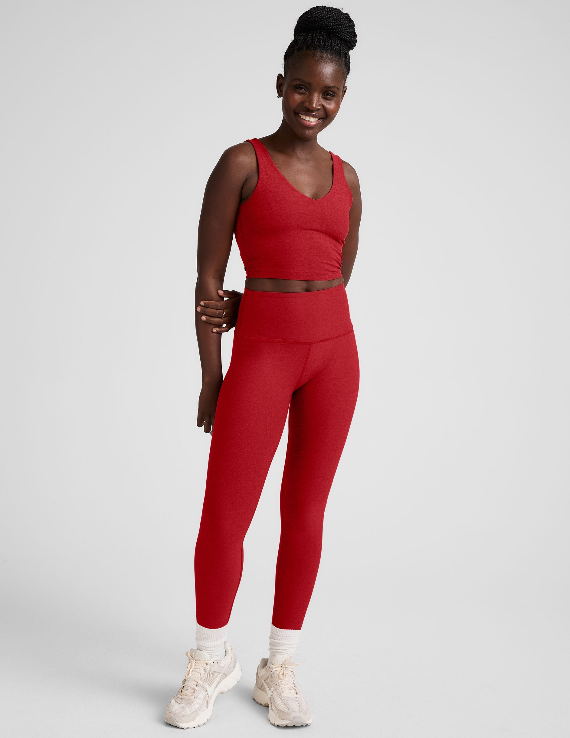 woman wearing a red v-neck cropped tank and leggings on a plain background.