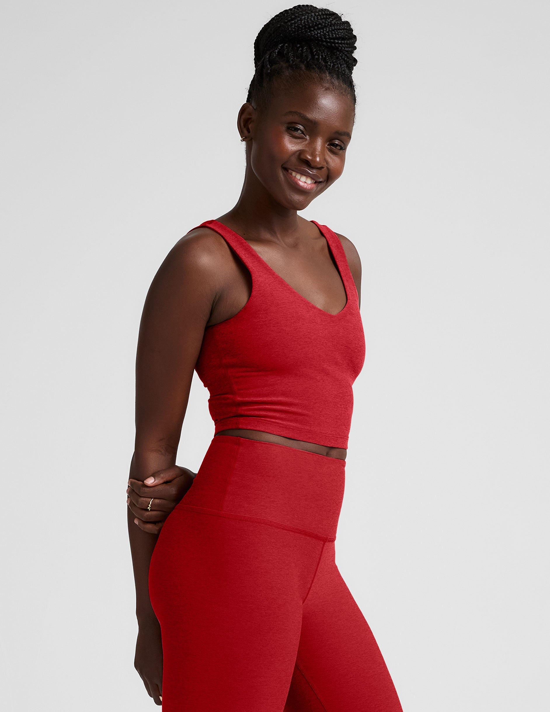 woman wearing a red v-neck cropped tank and leggings on a plain background.