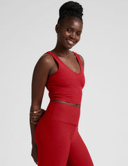 woman wearing a red v-neck cropped tank and leggings on a plain background.